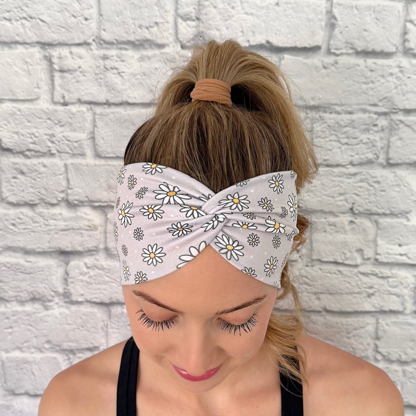 Woman with hair in ponytail wearing wide, twisted headband in gray with white daisy print.