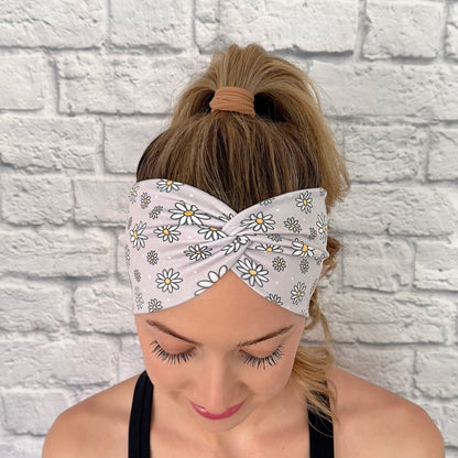 Woman with hair in ponytail wearing wide, twisted headband in gray with white daisy print.