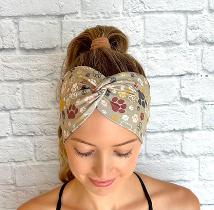 Woman with hair in ponytail wearing wide, twisted headband in green with multi-color dog paw print.
