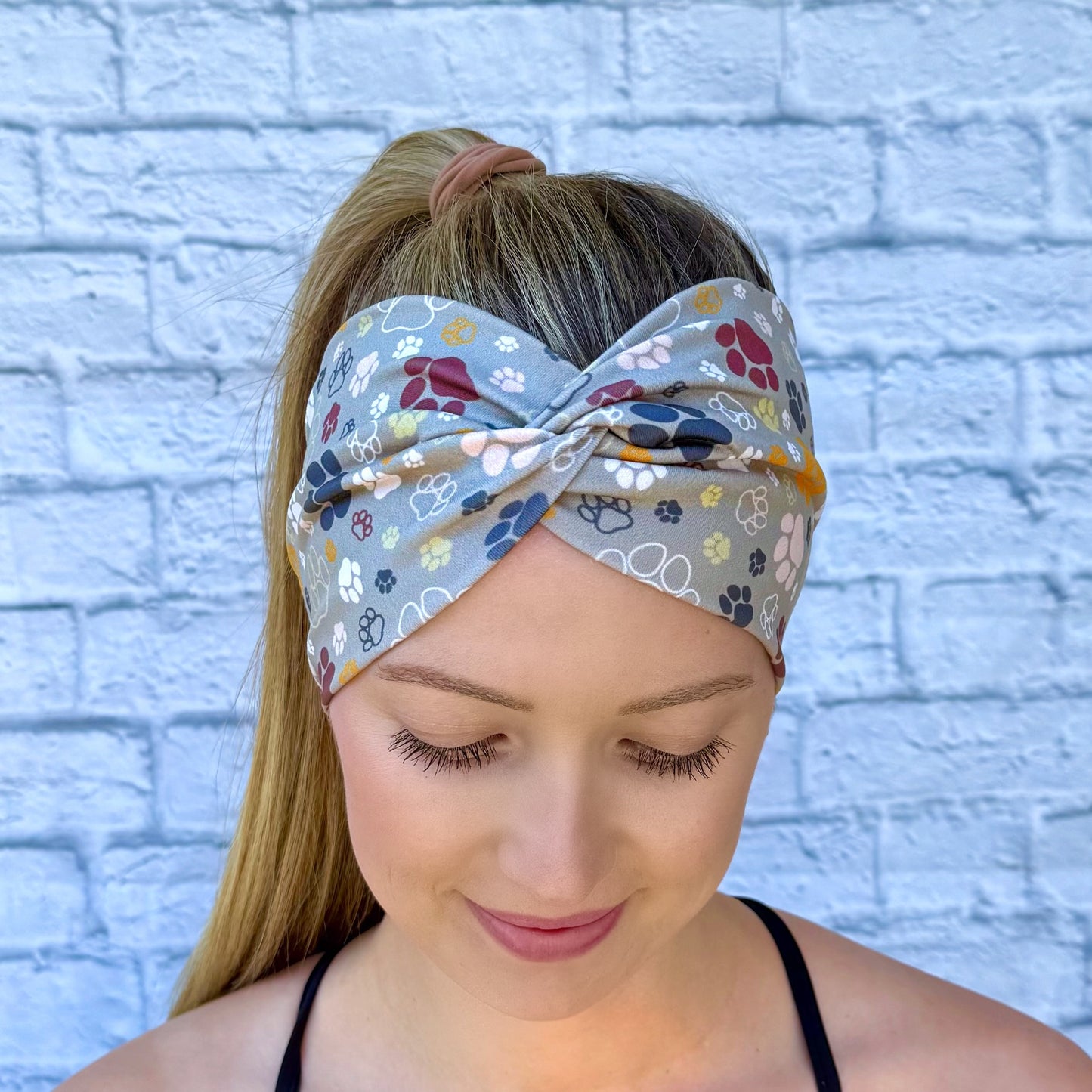Woman with hair in ponytail wearing wide, twisted headband in green with multi-color dog paw print.