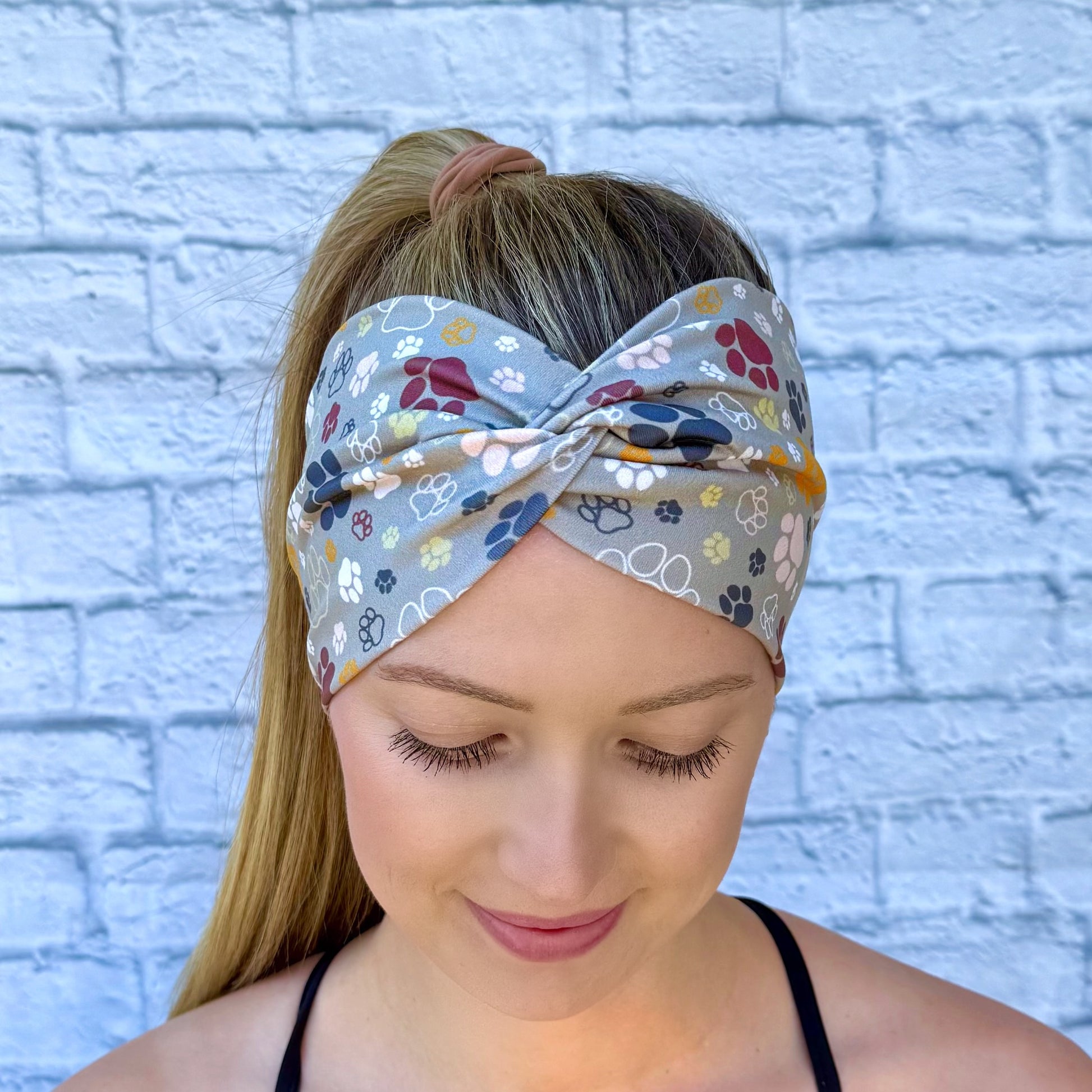 Woman with hair in ponytail wearing wide, twisted headband in green with multi-color dog paw print.