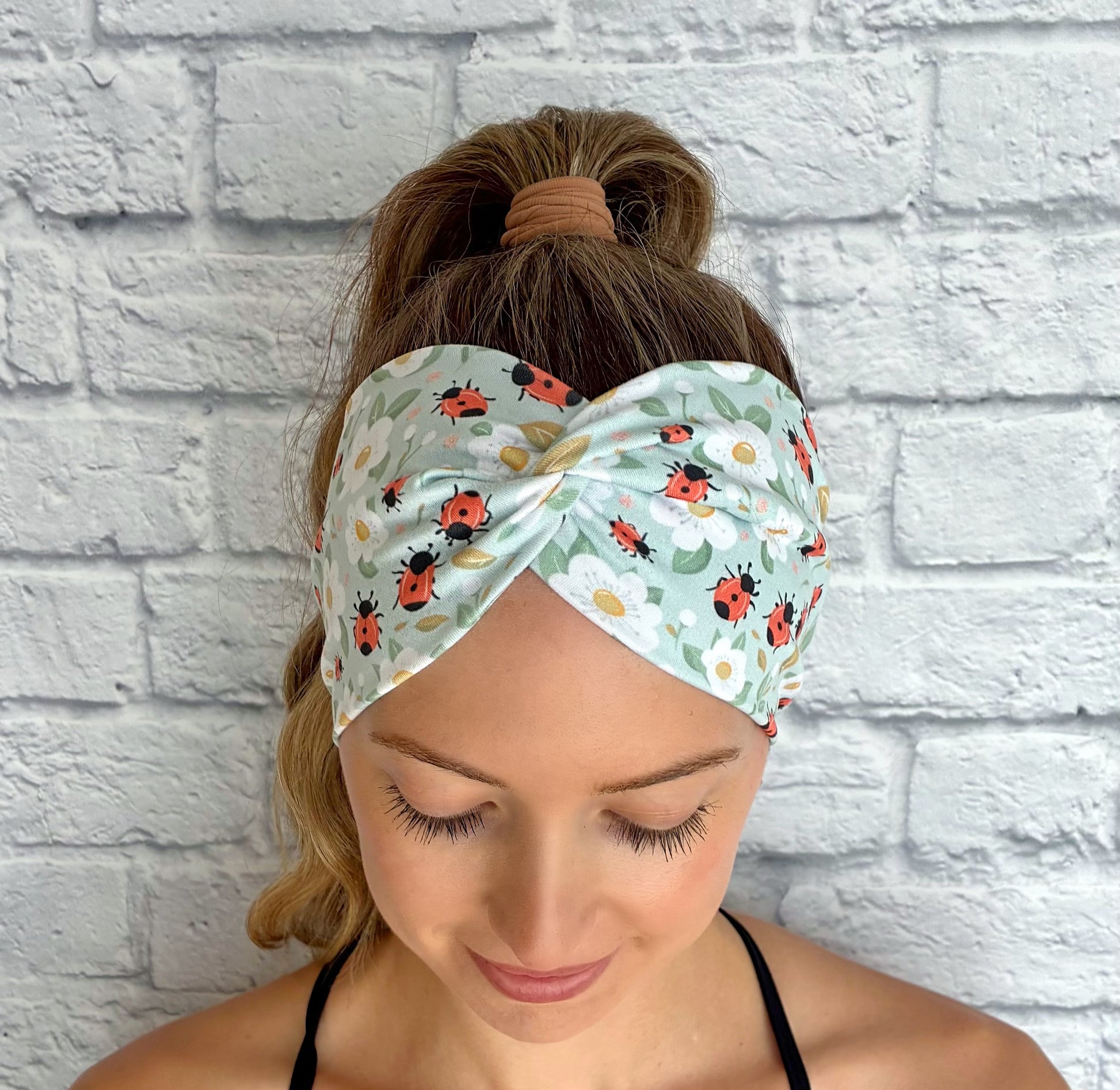 Woman wearing a headband with ladybug pattern against a white brick wall.