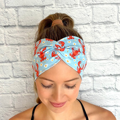 Woman with hair in ponytail wearing wide, twisted, light blue headband with lobster and white floral print.