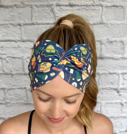 Woman with hair in curly ponytail wearing wide, twisted, navy blue headband with camping theme print.