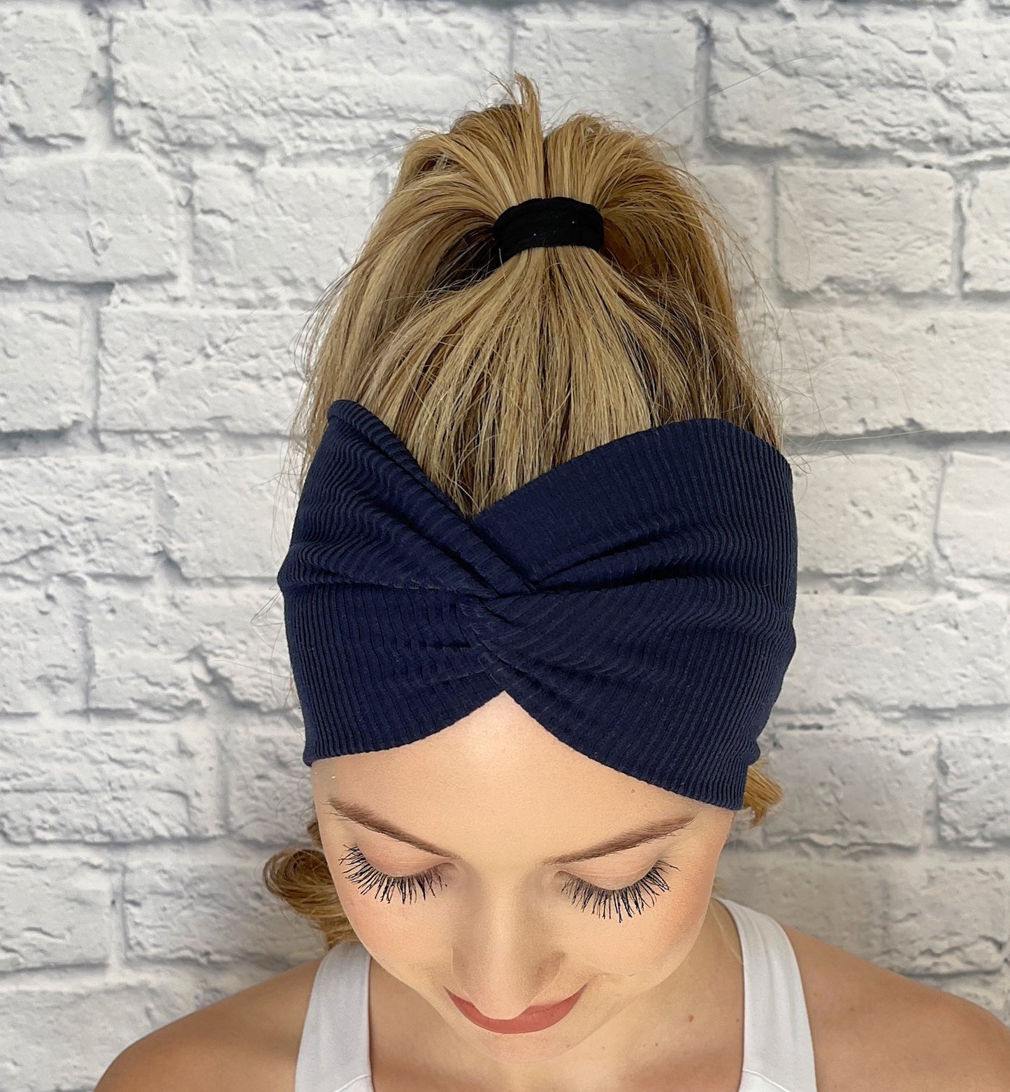 Woman with hair in curled ponytail wearing wide, twisted headband in navy blue ribbed material.