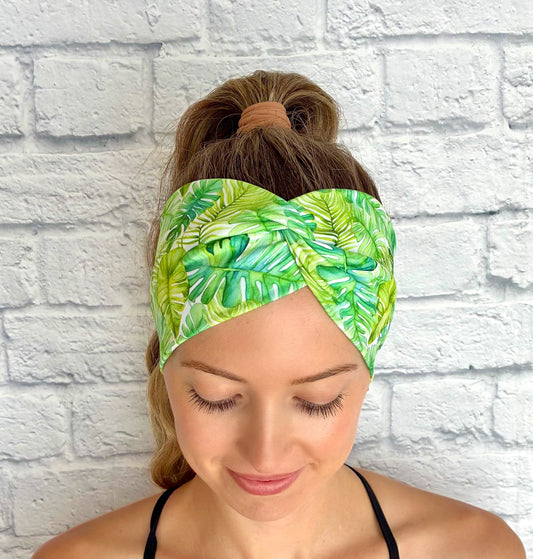 Woman wearing a green palm leaf-patterned headband against a white brick wall.