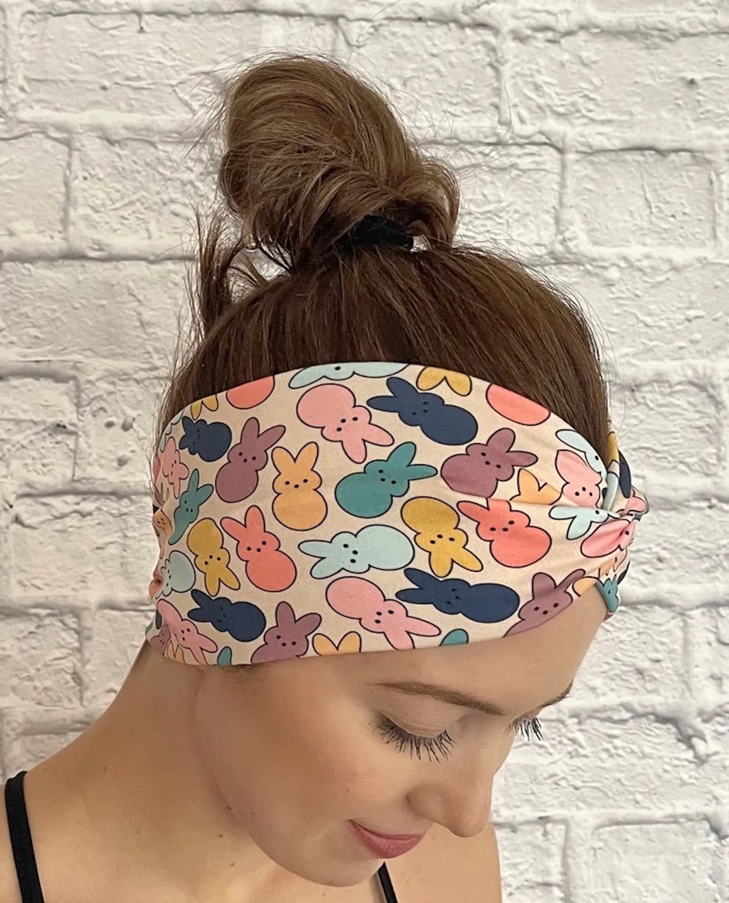 Woman with hair in bun wearing wide, twisted headband in peach/cream color with pastel print Easter bunnies.