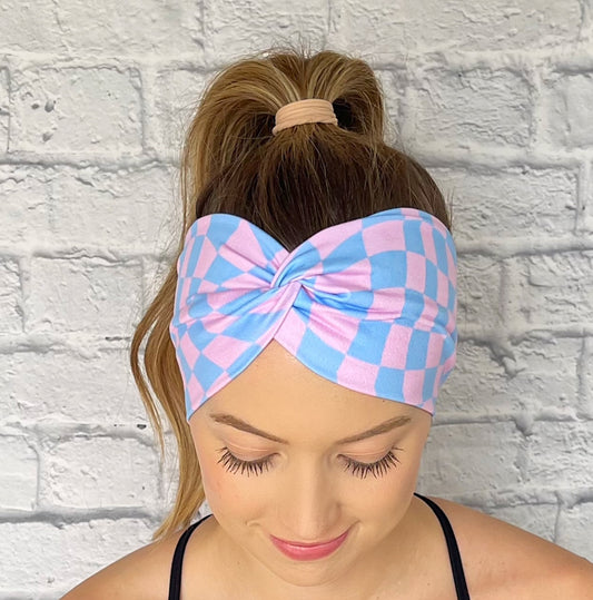 Woman with hair in curled ponytail wearing wide, twisted headband with pink and blue checker print.