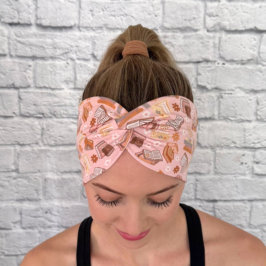 Woman wearing pink, wide twisted headband with books and flower print.