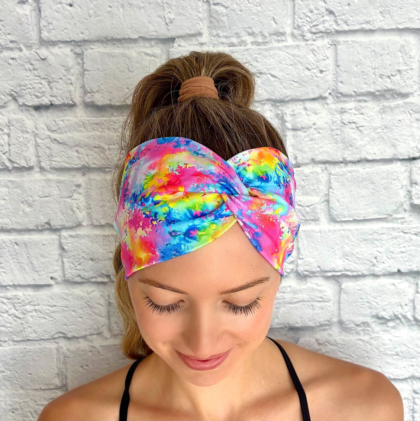 Woman wearing wide, twisted headband in rainbow color paint-splatter looking print.