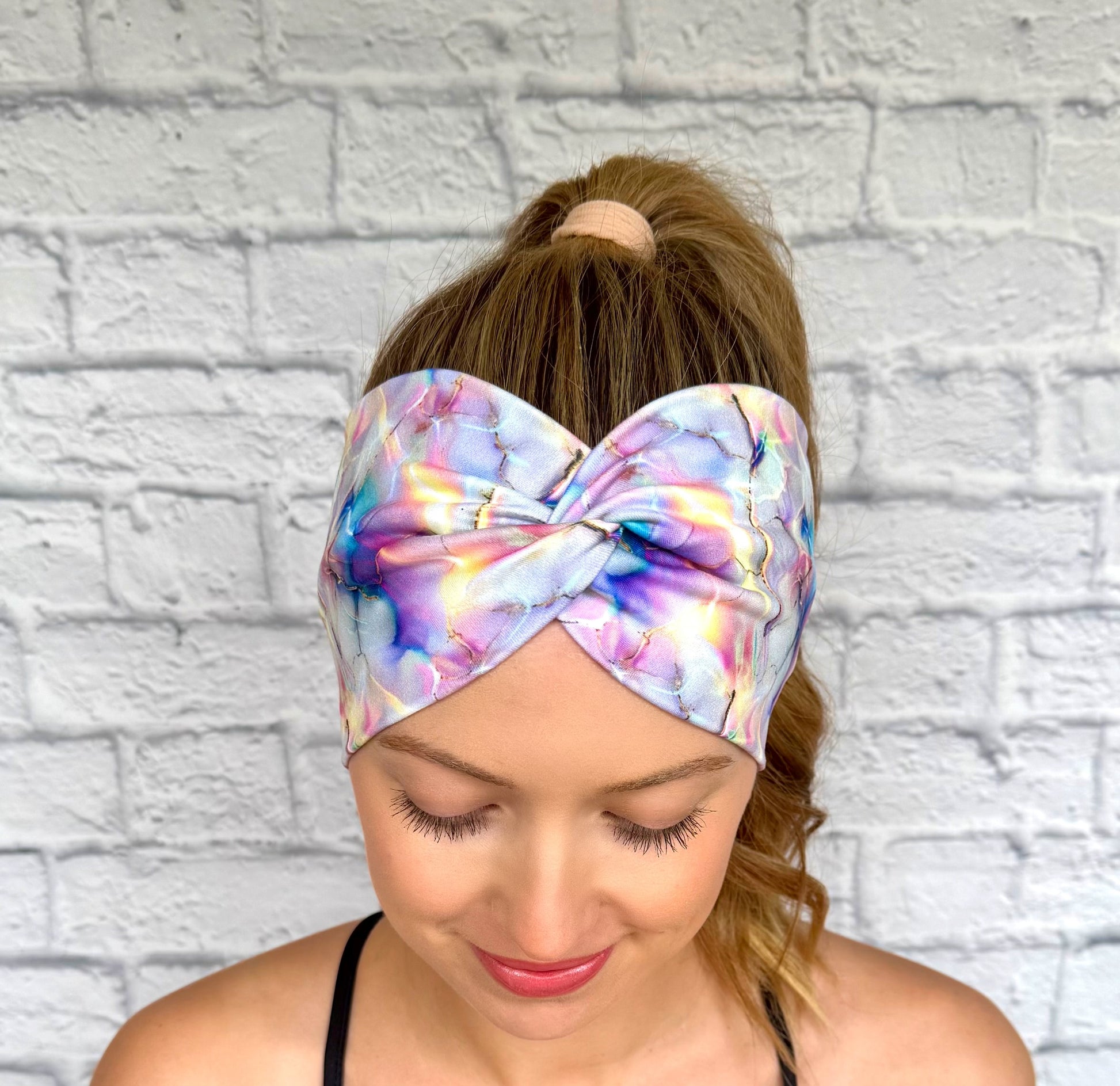 Woman with hair in ponytail wearing wide, twisted headband with multi-color watercolor print.