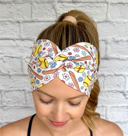 Woman with hair in ponytail wearing wide, twisted headband in cream color with softball and flower theme print.