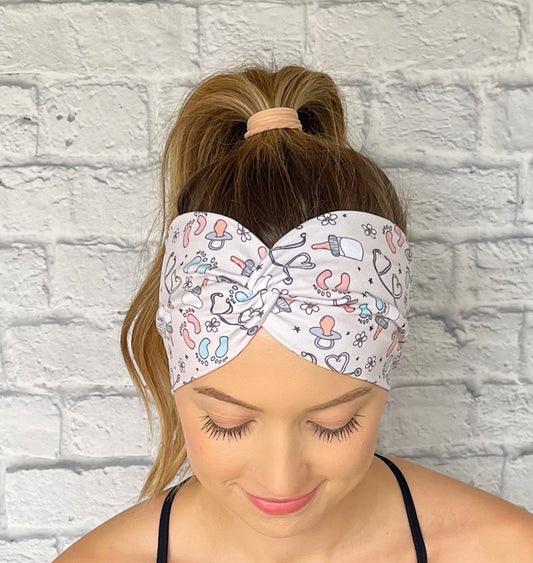 Woman wearing a tan, baby theme patterned headband against a white brick wall.