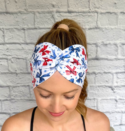 Woman with hair in ponytail wearing wide, twisted, white headband with red and blue bows and blue star print.