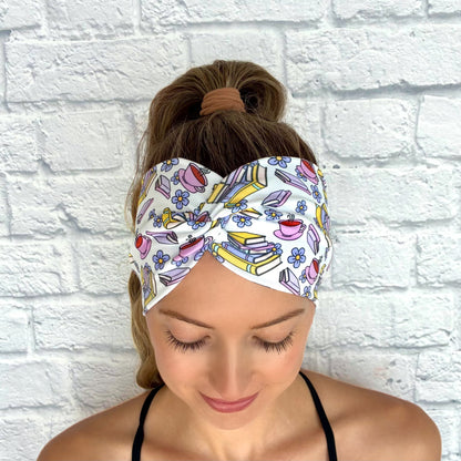 Woman with hair in ponytail wearing wide, twisted, white headband with coffee, flower, and book print.