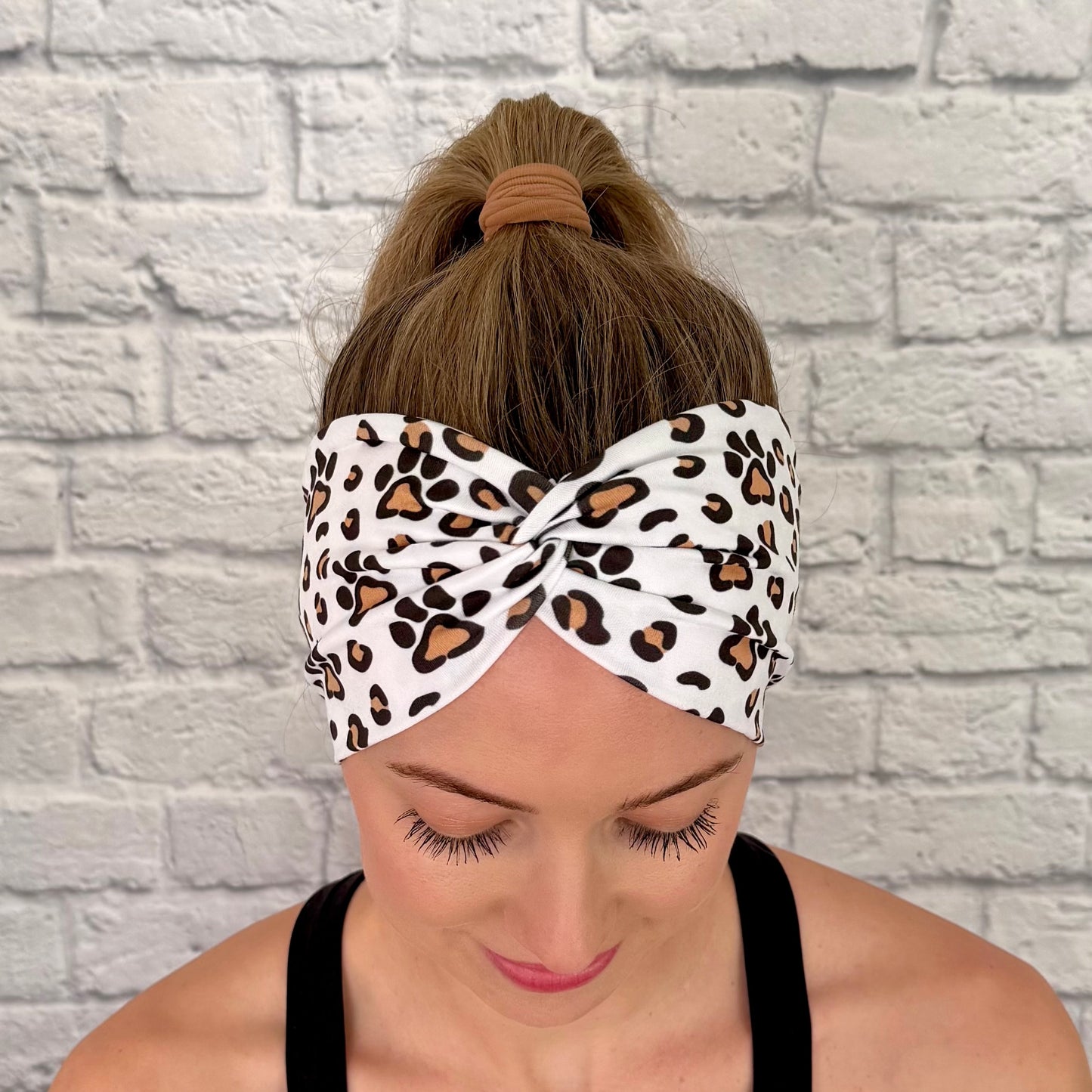 Woman with hair in bun wearing wide, white, twisted headband with brown and black dog paws and cheetah print.