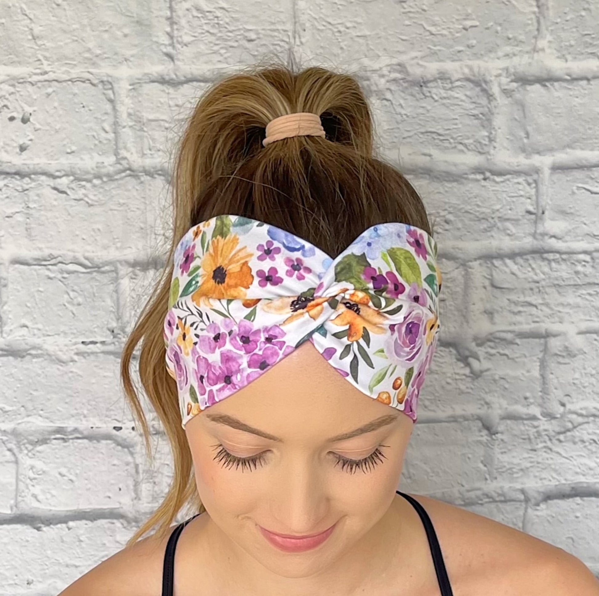 Woman wearing a colorful floral headband against a white brick wall.