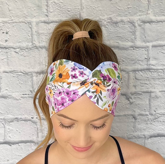 Woman wearing a colorful floral headband against a white brick wall.