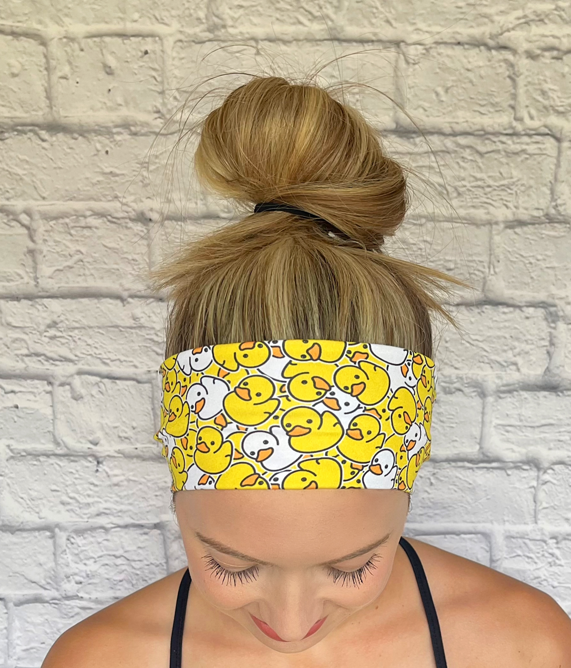 Woman with hair in bun wearing stretchy headband in yellow and white rubber duck print.