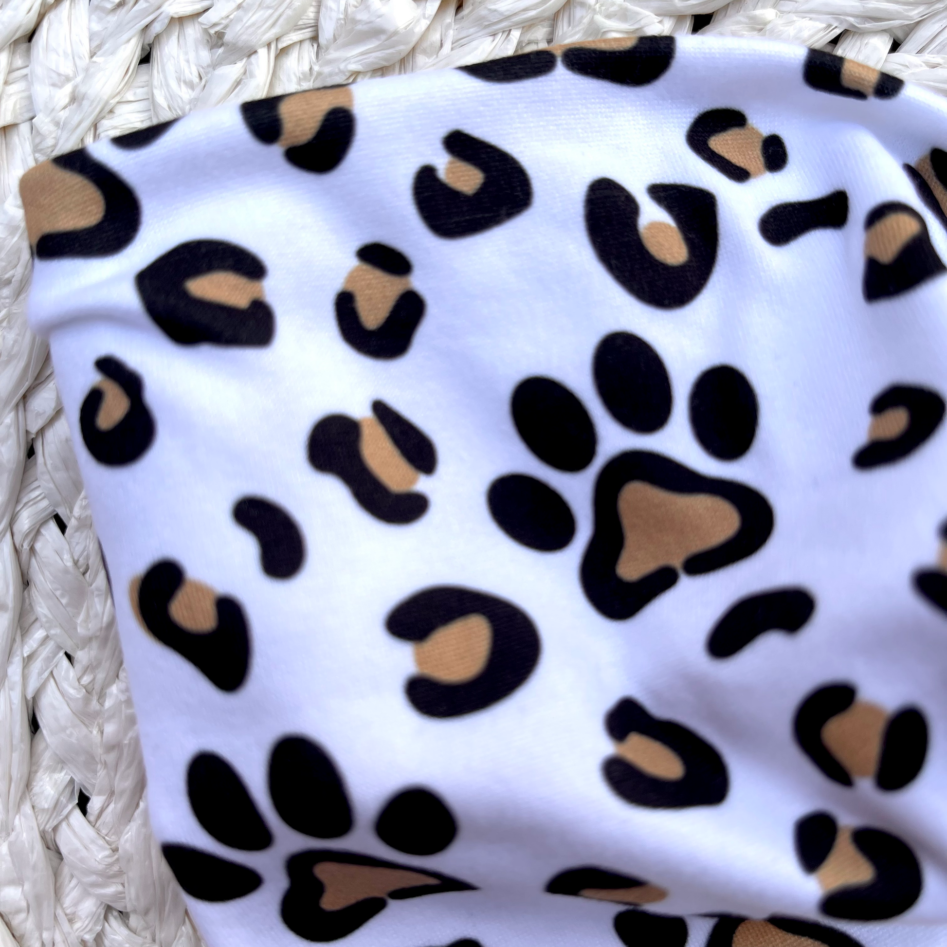 Wide, white, twisted headband with brown and black dog paws and cheetah print. 