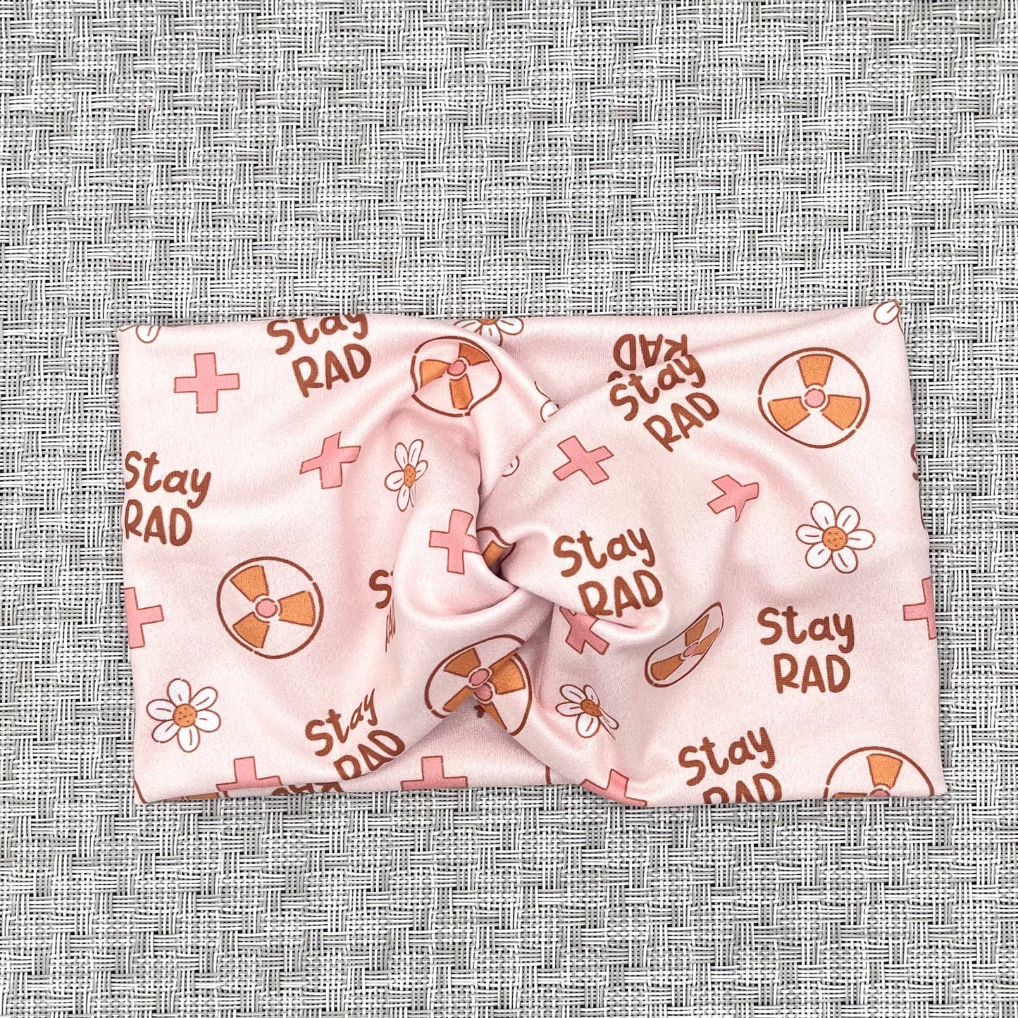 Twisted, wide headband in pink with "stay rad" print, radiology theme print, and flowers.