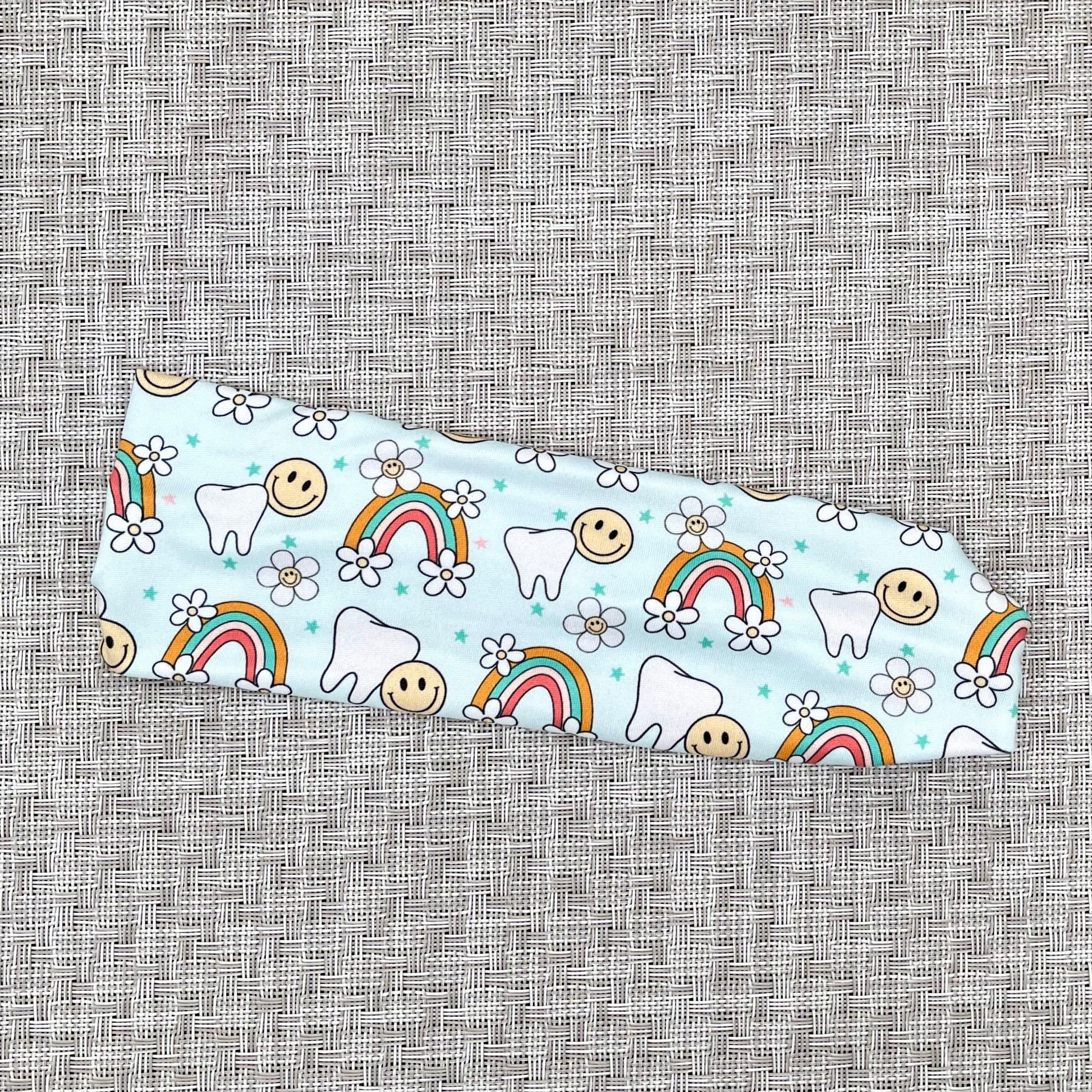 Light blue headband with teeth, rainbows, smiley faces, and flowers.