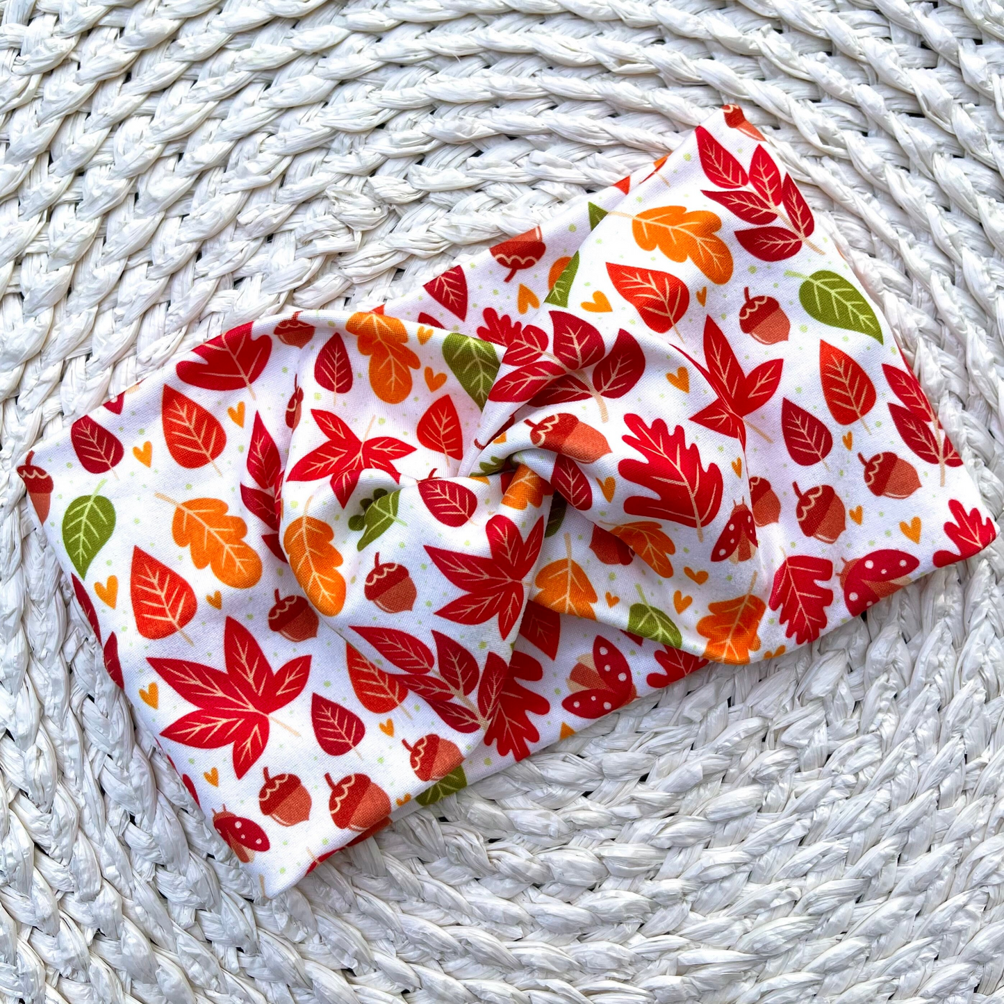 Wide, twisted, white headband with red, orange, and green leaves print.