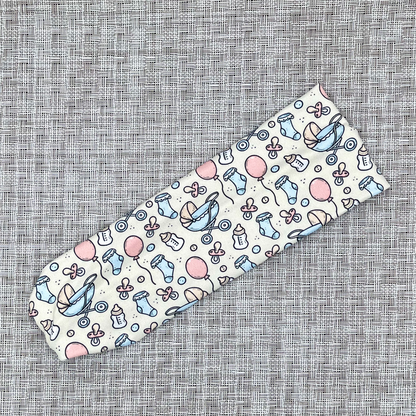 Baby-themed headband in cream color with blue, white, and pink on a textured gray background.
