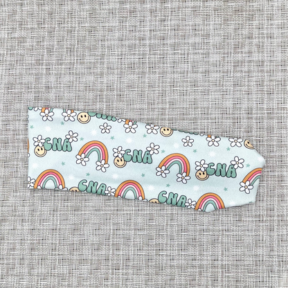 light blue headband with "cna" print, rainbows, white flowers, and smiley faces