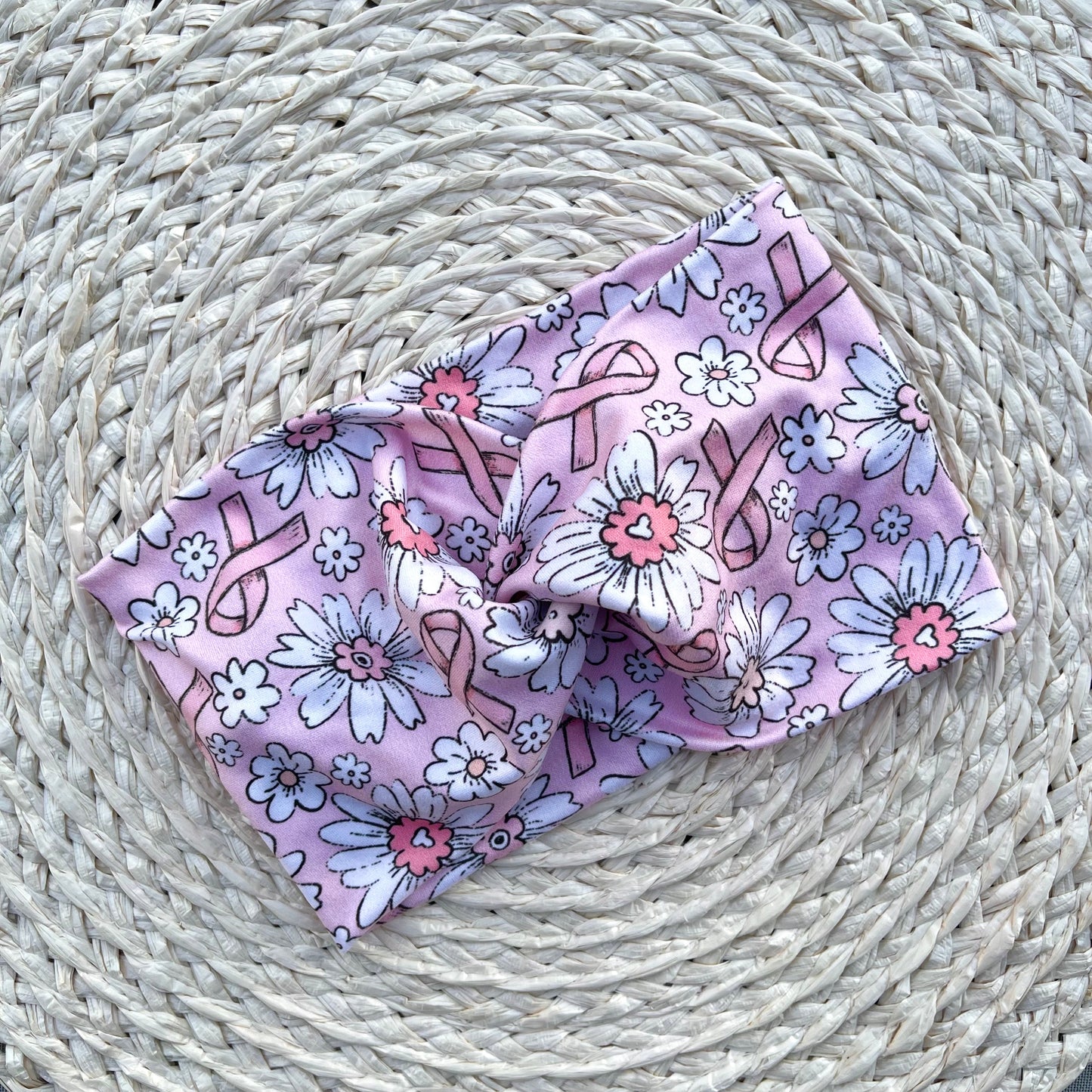 Light pink, wide, twisted headband with pink ribbon and white flower print.