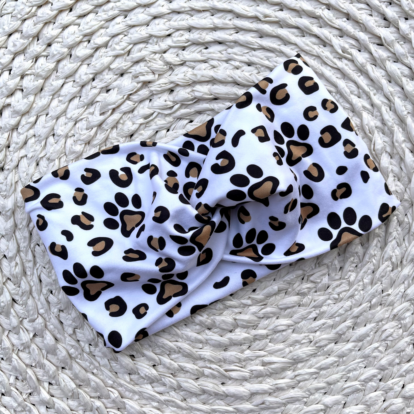 Wide, white, twisted headband with brown and black dog paws and cheetah print. 