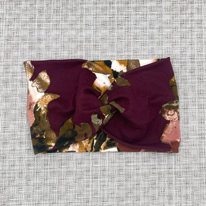 Wide, twisted headband in maroon color with pink and gold flowers.