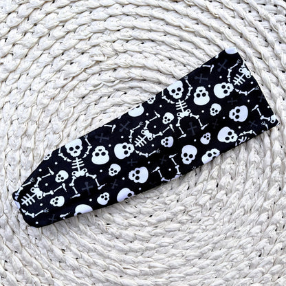 Black headband with white skull and skeleton pattern on a woven white surface
