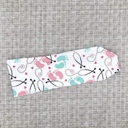 Baby-themed headband with stethoscope, footprints, and hearts on a gray background