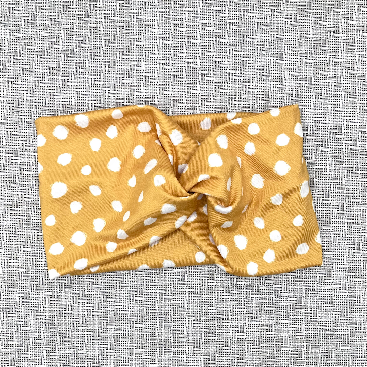 Wide, twisted headband in gold color with white spots.