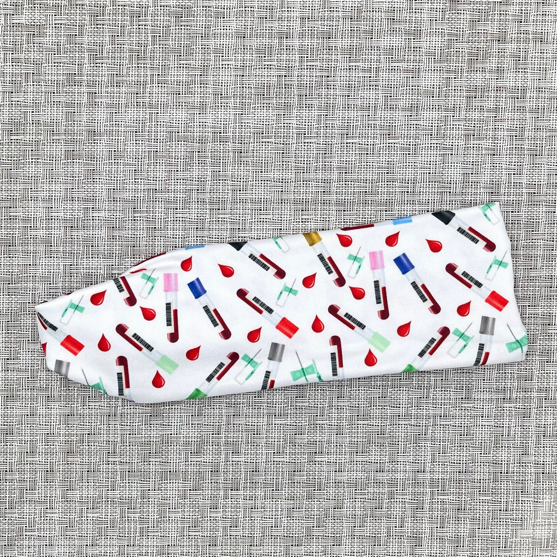 white headband with phlebotomy theme print- blood vials, blood drops, and syringes