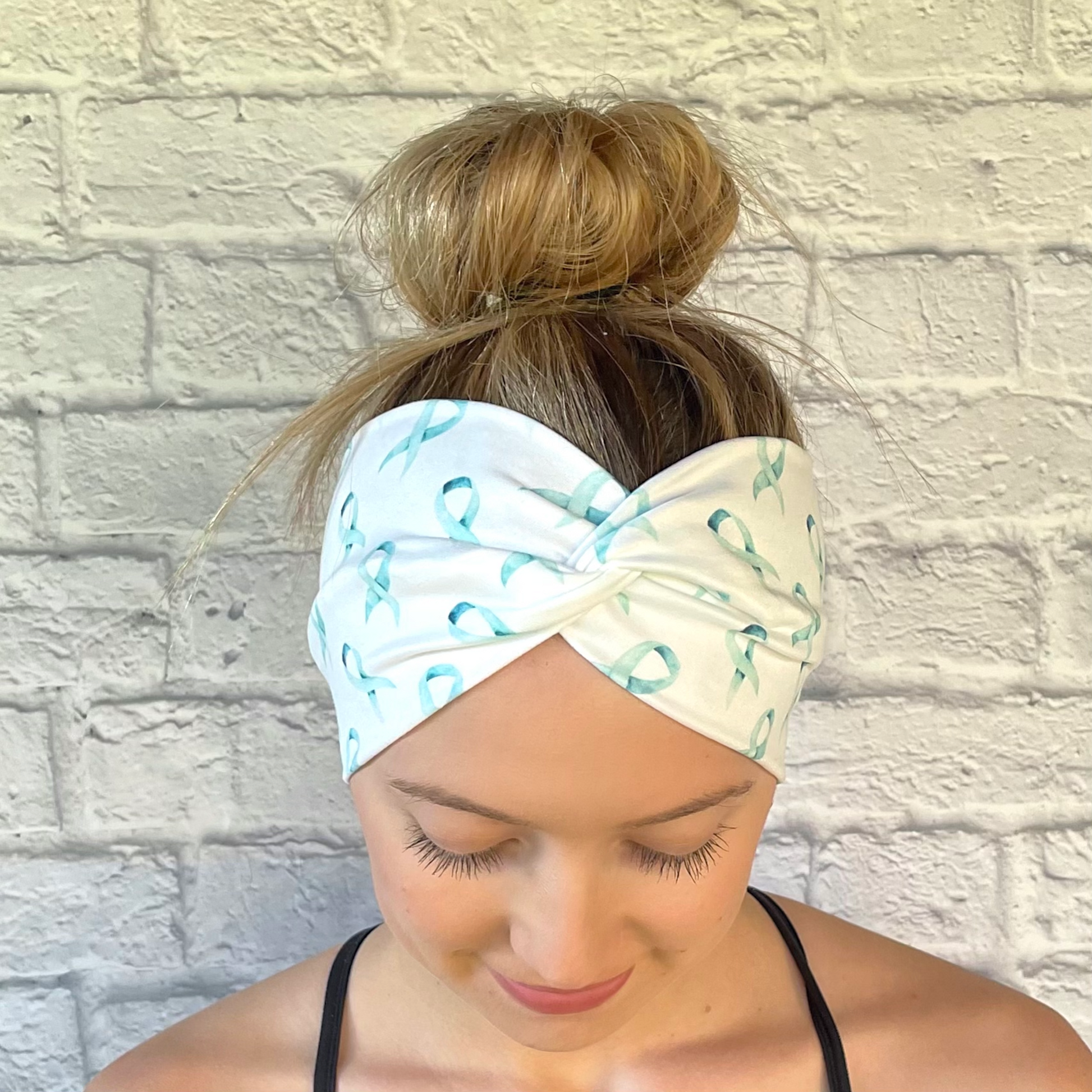 Woman with hair in bun wearing wide, white, twisted headband with light blue ribbon print.