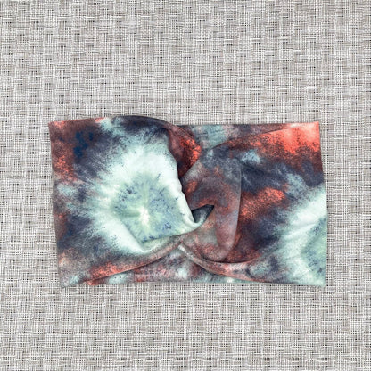 Wide, twisted headband in tie dye print with peach, white, light blue, and dark gray/blue.