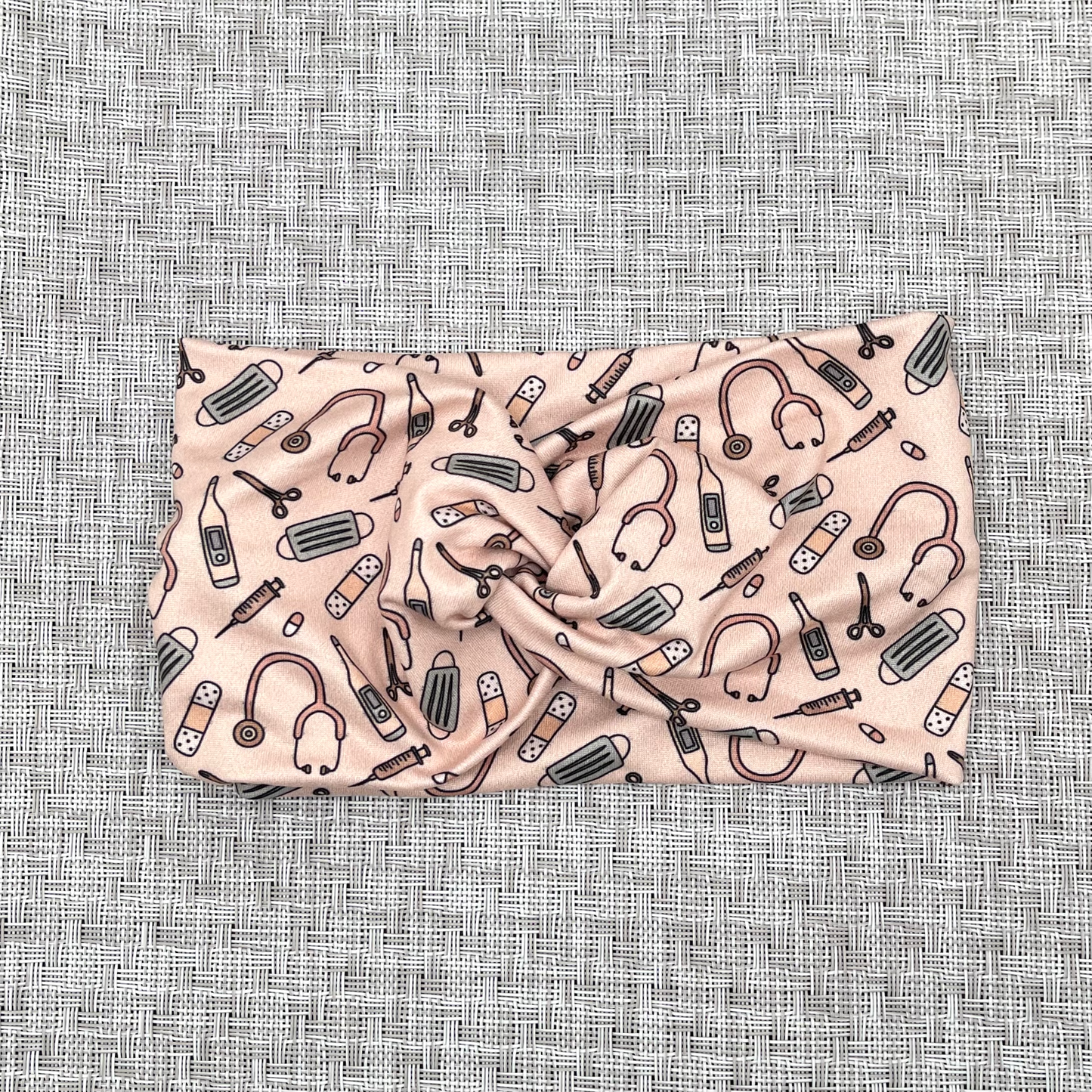 Wide, twisted headband in peach color with medical theme print.