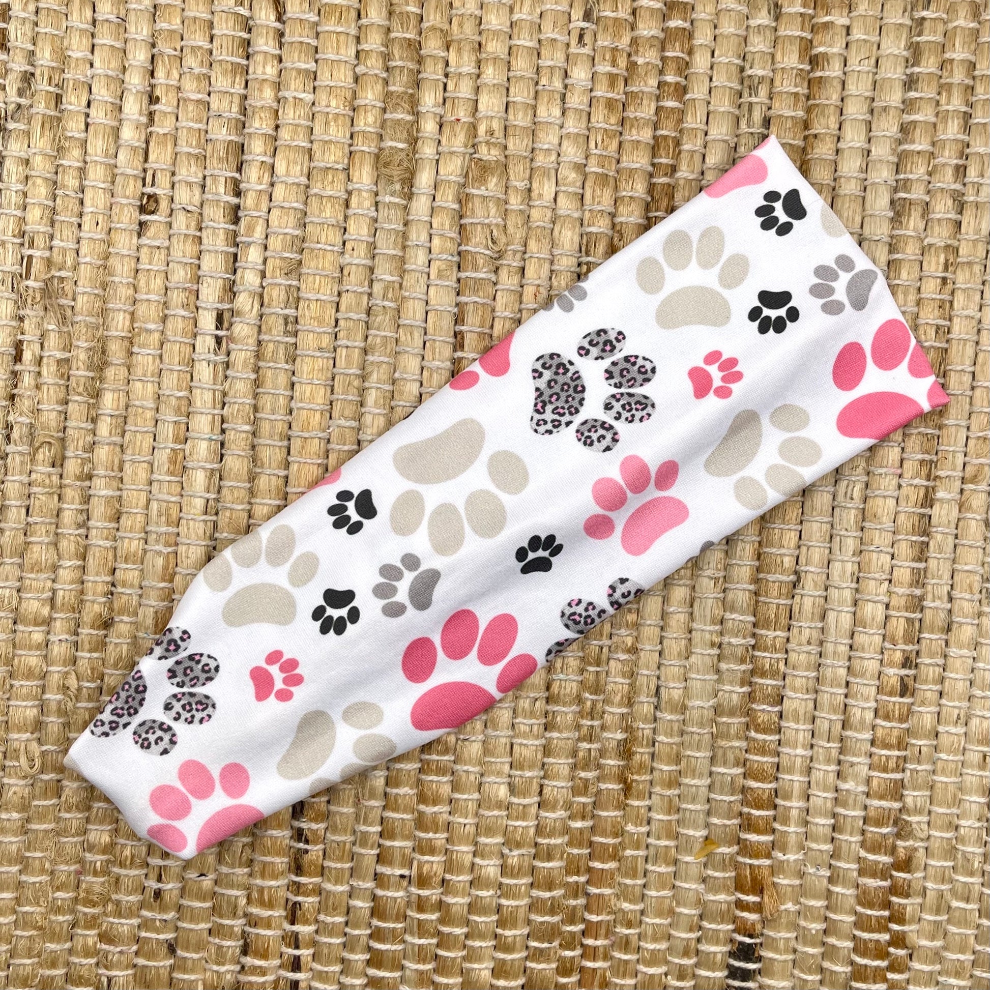 Flat, stretchy headband in white with pink, gray, and black paw print.