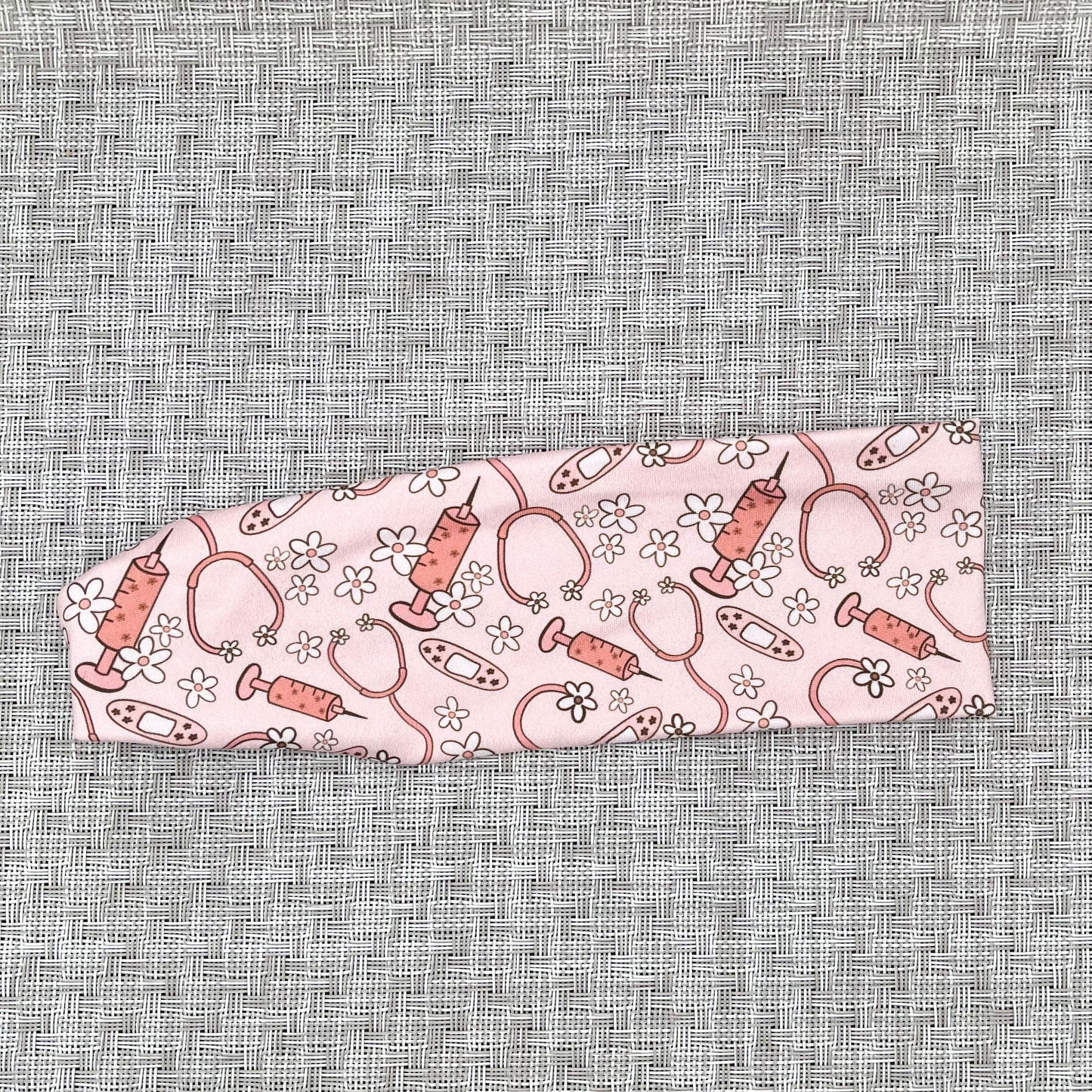 Pink headband with pink and white medical theme print- stethoscopes, bandages, syringes, and flowers.