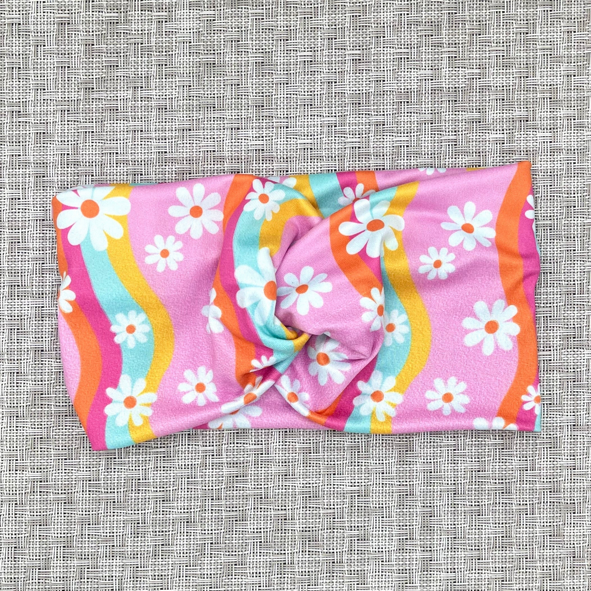 Wide, twisted headband in light pink with white flower and swirl print in light blue, yellow, dark pink, and orange.