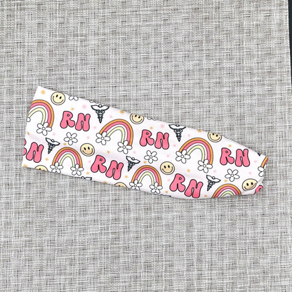 Stretchy, light pink headband with "RN", rainbows, flowers, and smiley faces