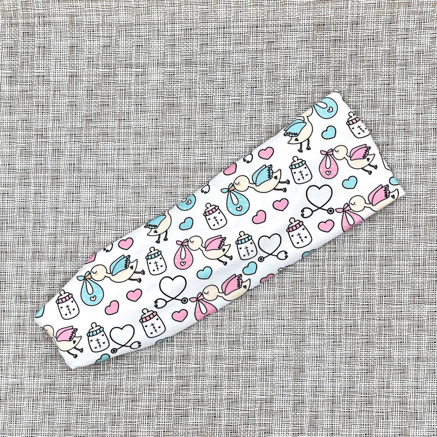 White, stretchy headband with baby theme print- storks, hearts, bottles, and stethoscopes.