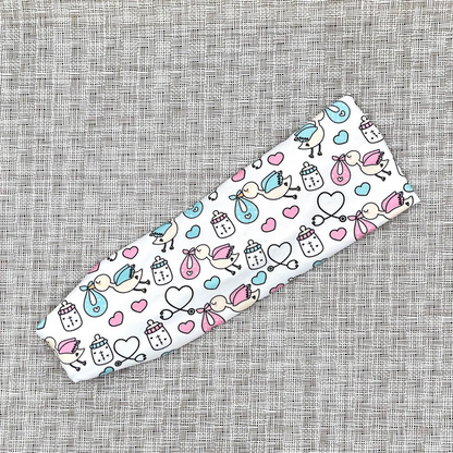 White, stretchy headband with baby theme print- storks, hearts, bottles, and stethoscopes.