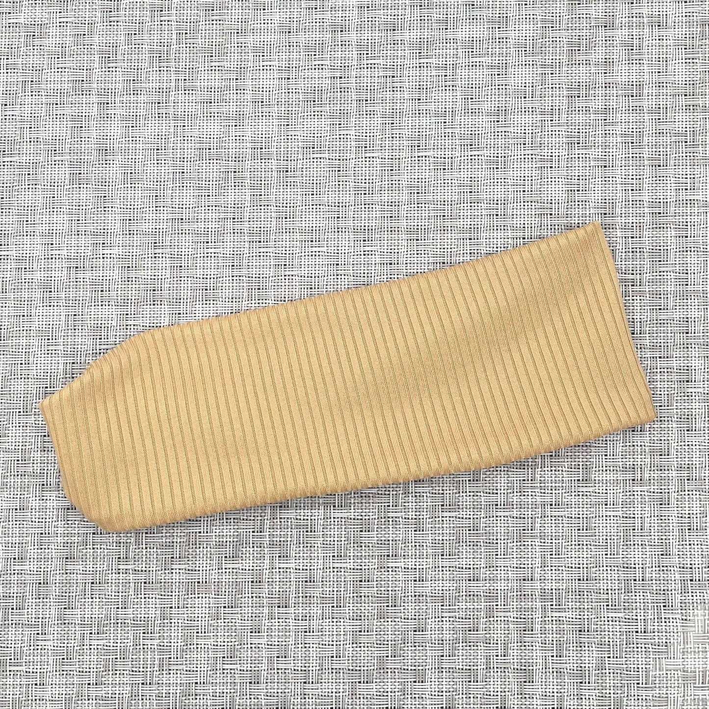 Flat, stretchy, tan color ribbed headband on gray background.