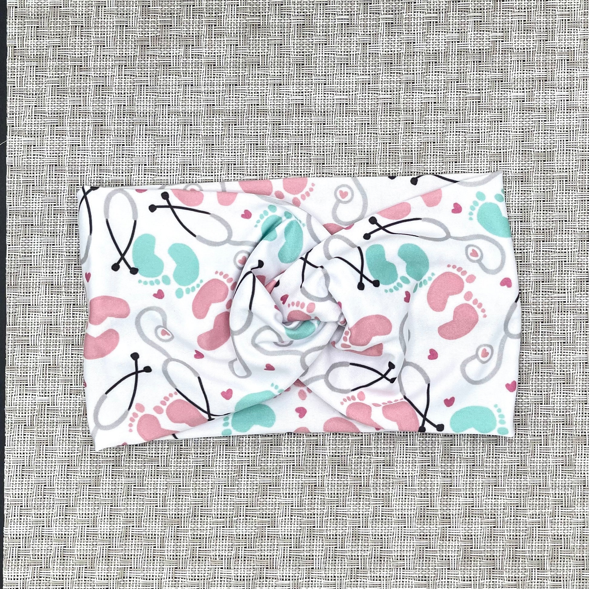 Baby-themed fabric headband with stethoscopes, hearts, and footprints on a gray background