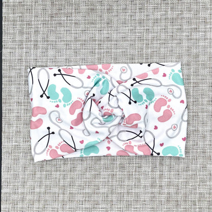 Baby-themed fabric headband with stethoscopes, hearts, and footprints on a gray background
