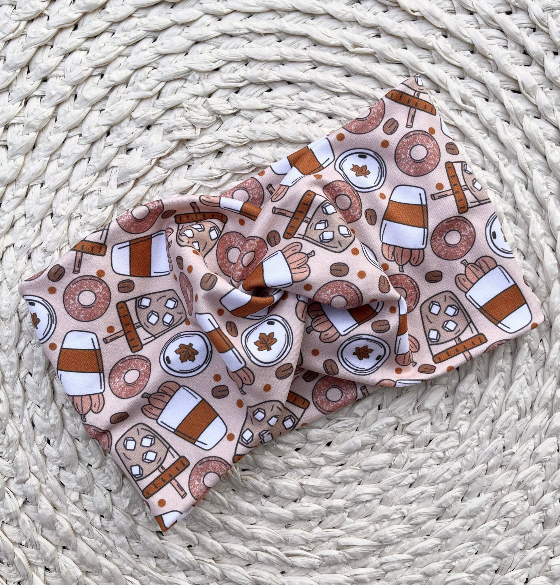 Wide, twisted, fall theme, pumpkin spice patterned headband against a cream patterned background