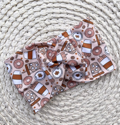 Wide, twisted, fall theme, pumpkin spice patterned headband against a cream patterned background